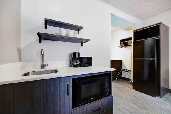 A modern kitchen with a sink, microwave, coffee maker, and black cabinets.
