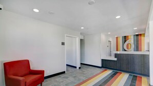 A hotel lobby with a red armchair, a reception desk, and a colorful striped carpet.