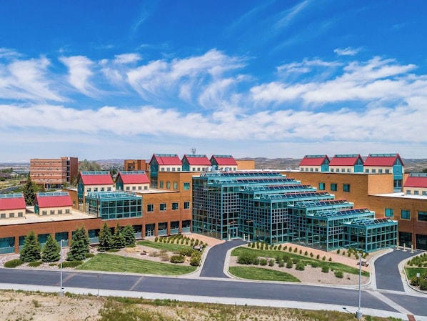 A modern building with multiple red-roofed sections, a central glass structure, and a landscaped courtyard.