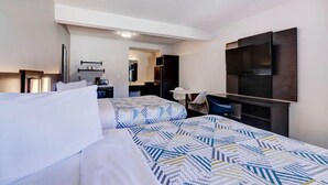 A hotel room with two beds, a desk, a chair, a TV, and a kitchenette.