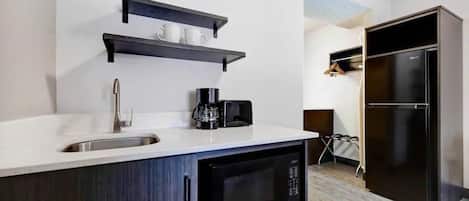A modern kitchen with a sink, microwave, coffee maker, and black cabinets.