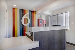 A reception desk with a large number '6' on the wall, a refrigerator, and a window with blinds. - 4 Clean Modern Rooms Ideal for Exploring Wyoming’s Scenic Sites | Free Breakfast (Rock Springs)