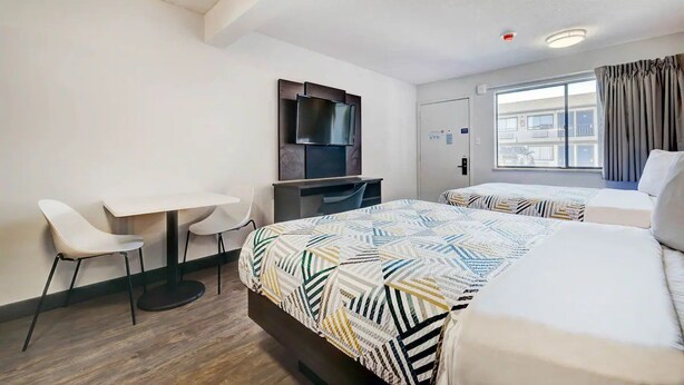 Ein Hotelzimmer mit zwei Betten, einem Schreibtisch, einem Stuhl, einem Fernseher und einem Fenster mit Vorhängen.