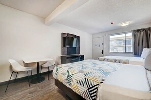 Habitación de hotel con dos camas, un escritorio, una silla, un televisor y una ventana con cortinas.