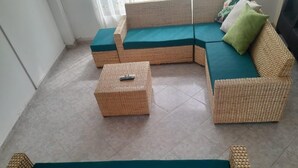 Un conjunto de sofá de mimbre con cojines azul turquesa, una mesita de mimbre con un control remoto, y una alfombra verde.