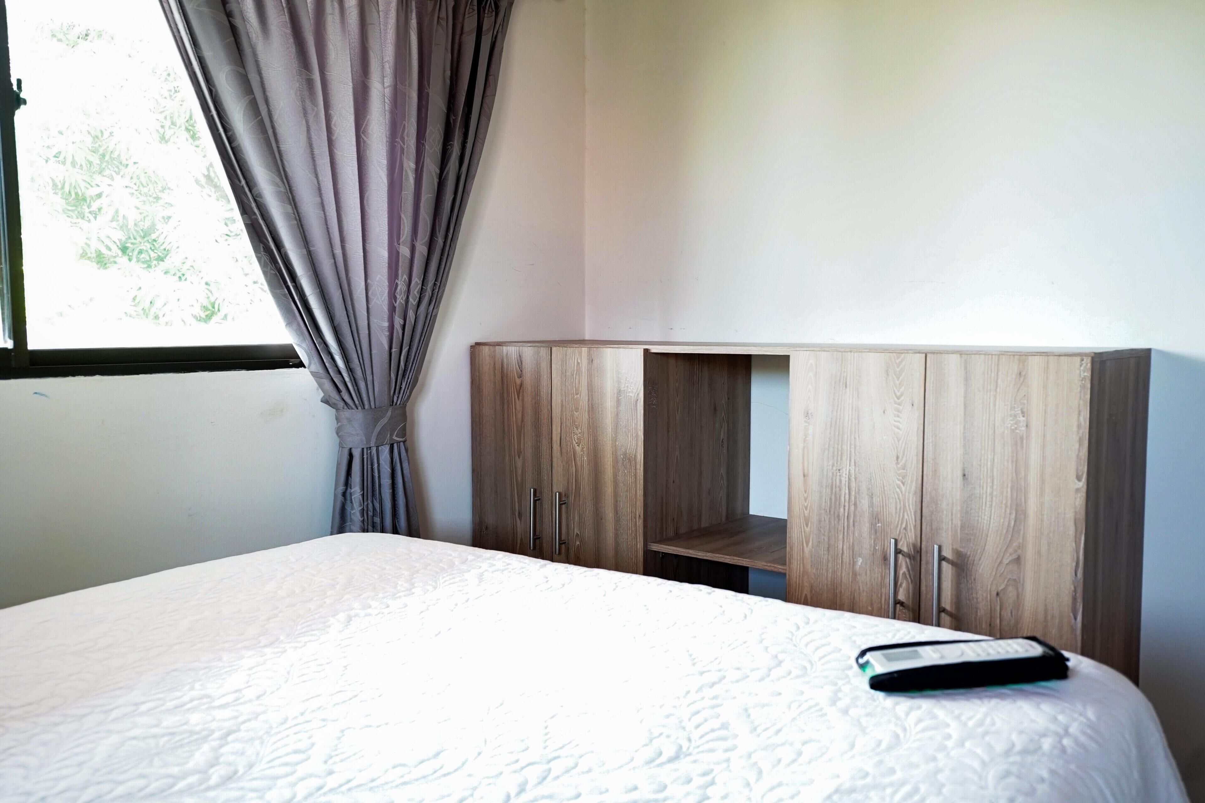 A room with a bed, a wooden wardrobe, and a window with curtains.