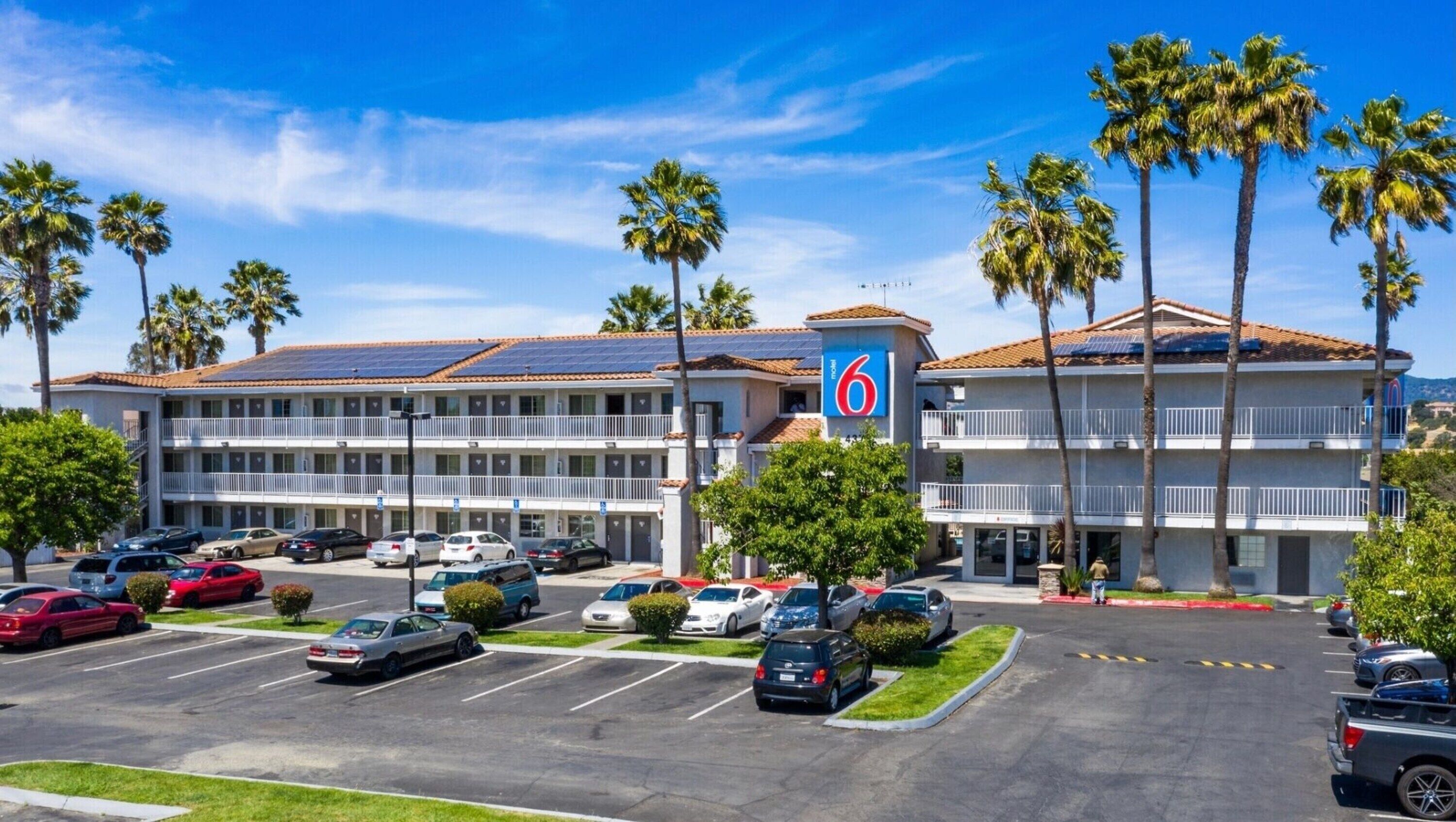 A motel with a parking lot, multiple cars, and palm trees.