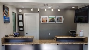A reception area with a closed door, framed certificates, a computer monitor, granite countertops, and a flat-screen TV.