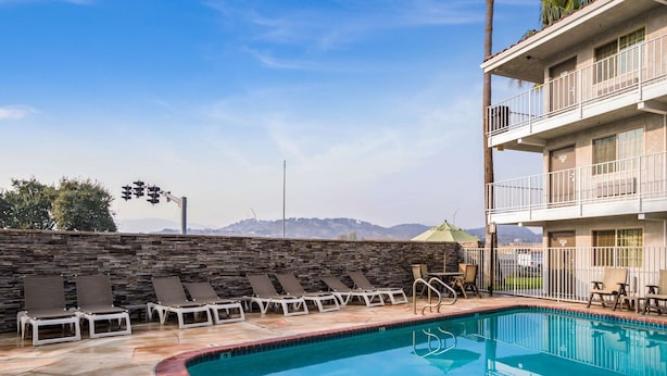Una piscina con sillas de descanso, un muro de piedra y vistas a montañas.