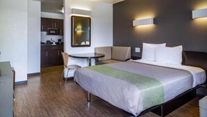 A hotel room with a bed, a desk, a chair, a microwave, and a small kitchenette.