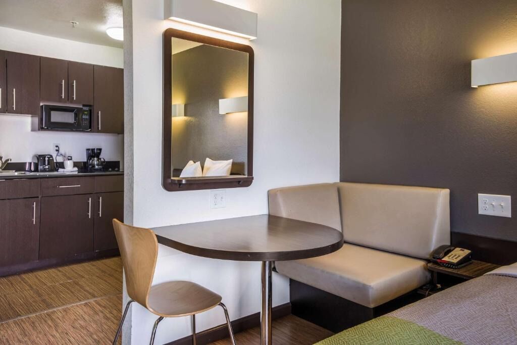 A hotel room with a kitchenette, a round table, a sofa, and a mirror.