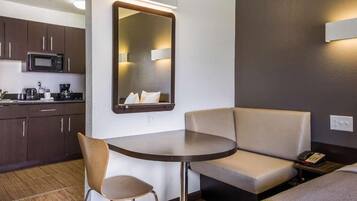 A hotel room with a kitchenette, a round table, a sofa, and a mirror.