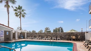 A swimming pool with lounge chairs, a stone wall, and palm trees. - 4 Convenient Rooms for Restful Stays | Pet-Friendly | Solano Town Center -5.4 mi (Fairfield)