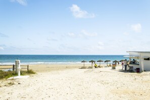 Ein Strand mit einer Kiosk, Sonnenschirmen und einem Holzzaun.