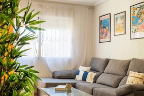 Ein Wohnzimmer mit grauem Sofa, einem Glastisch, einem Buch und einer Pflanze.