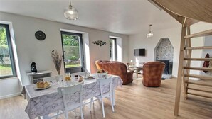 Un comedor con una mesa de mármol, sillas blancas, una chimenea y una escalera de madera.