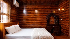 A room with wooden panel walls, a bed with white bedding, a wooden dresser, and a mirror.