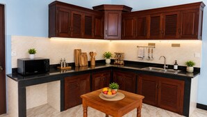 Una cocina con armarios de madera oscura, una encimera negra, un microondas, un lavabo y una mesa de madera con un frutero.