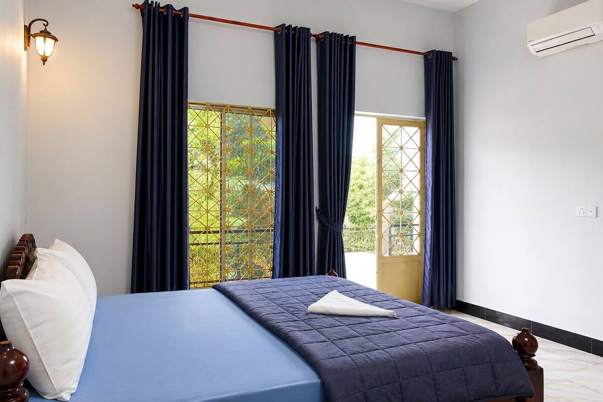 Un dormitorio con cama, ventana con cortinas, unidad de aire acondicionado y lámpara fijada a la pared.