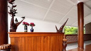 A wooden reception desk with a white ceiling and a view of greenery outside.