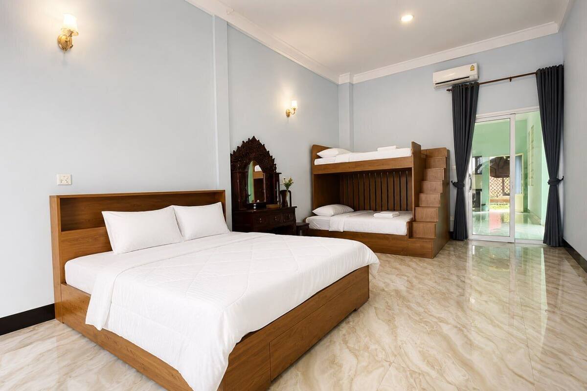 Una habitación de hotel con una cama grande, una cama más pequeña, un tocador con espejo y vistas al exterior a través de una puerta de cristal.