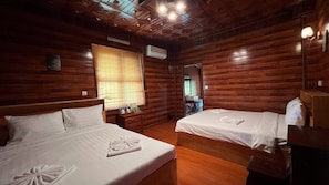 Quarto com duas camas, paredes de madeira, teto com padrão geométrico e janela com persianas.