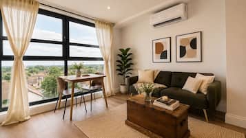 A living room with a sofa, a coffee table, a dining table with chairs, and a large window with curtains.
