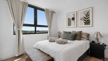 A bedroom with a large bed, two bedside tables, a bench, a window with curtains, and two wall-mounted artworks.