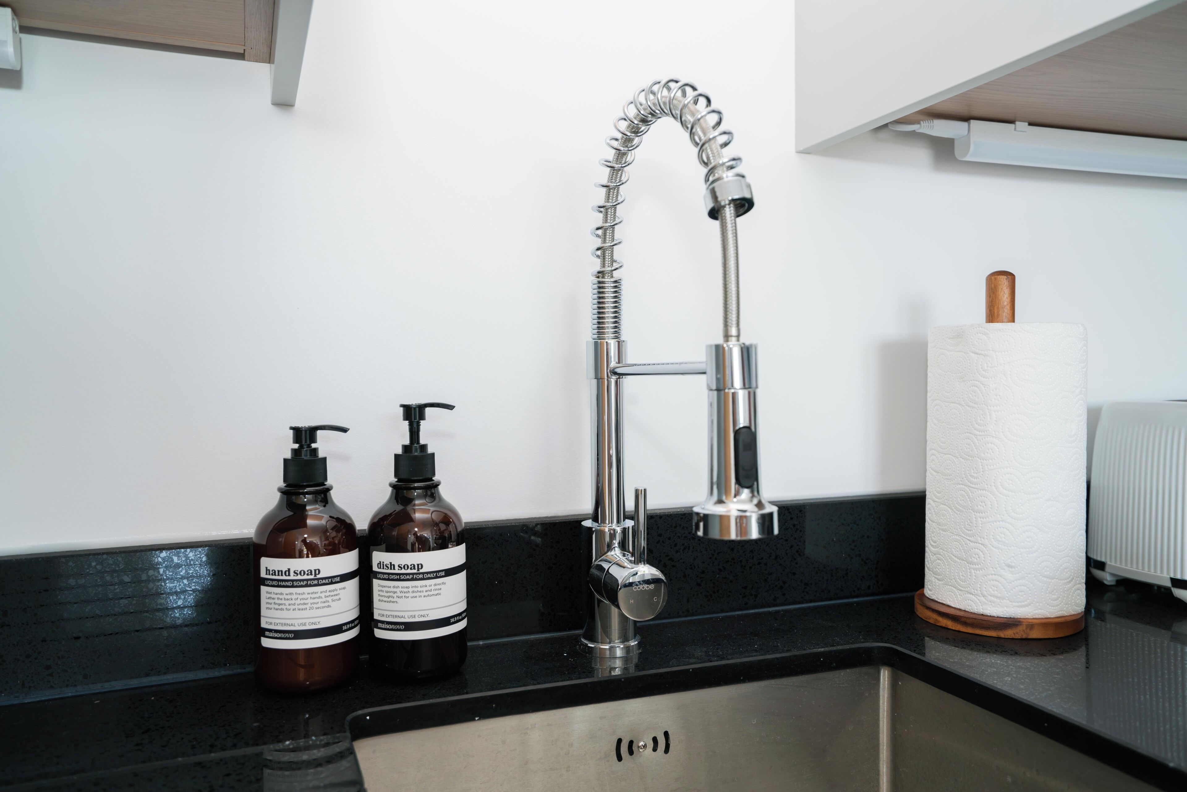 A kitchen sink with a modern faucet, two bottles of soap, and a paper towel holder.