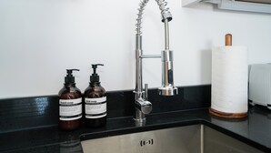 Ein Küchenspülbecken mit einem modernen Wasserhahn, zwei Seifenflaschen und einem Papierhandtuchhalter.