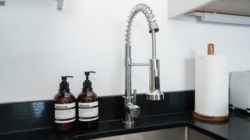 A kitchen sink with a modern faucet, two bottles of soap, and a paper towel holder.