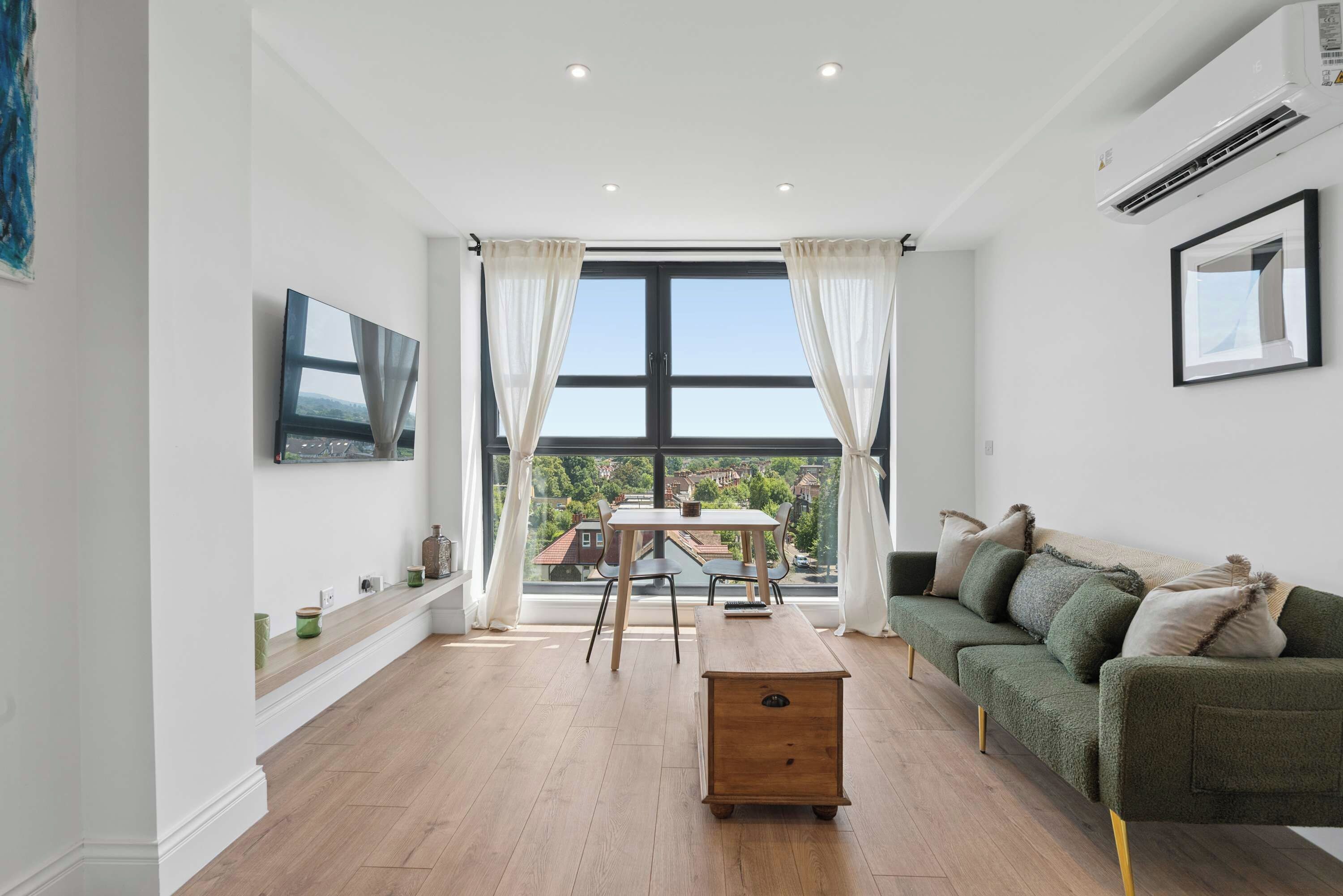 A modern living room with a dining area, large windows, and a green sofa.