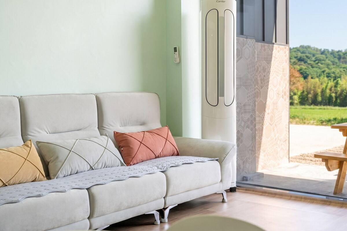 Ein modernes Wohnzimmer mit einer Couch, Kissen, einer Glastür, die nach draußen führt, und Blick auf eine grüne Landschaft.
