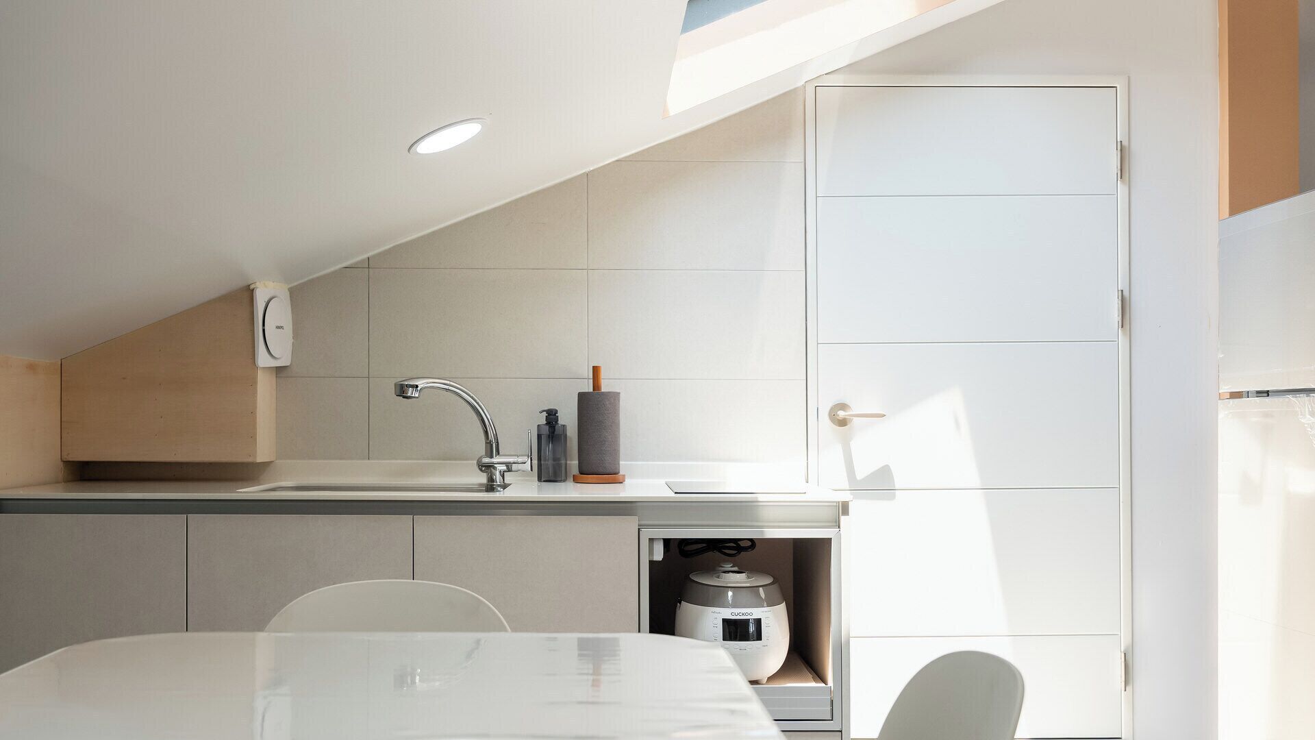 Una cocina moderna con lavavajillas integrado, un lavabo con grifo y un refrigerador compacto.