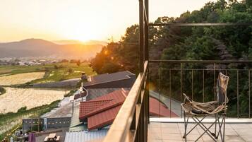 A balcony with a view of a sunset over a landscape, a hammock, and a small table.
