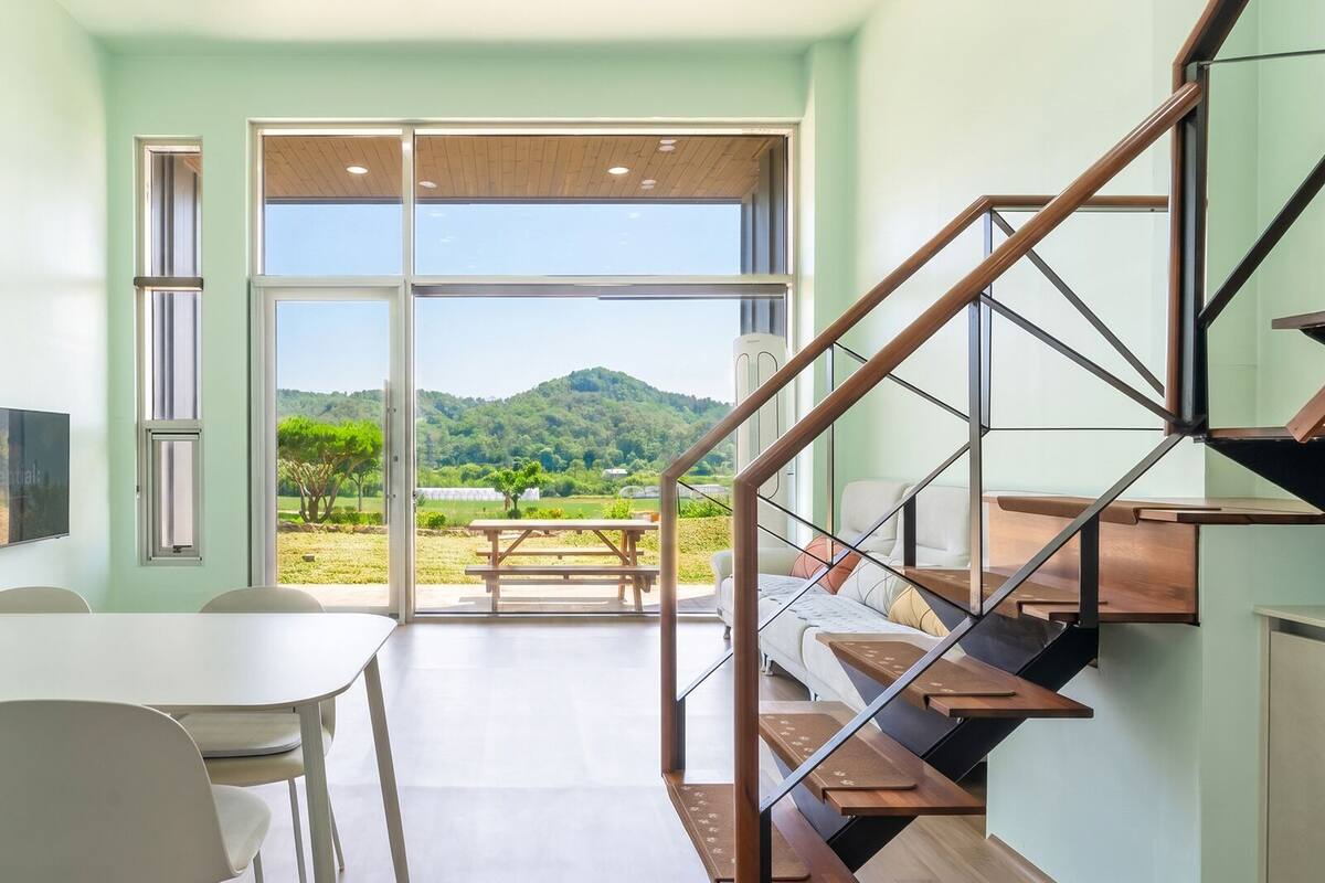 Ein modernes Interieur mit Essbereich, Treppe und Blick auf eine grüne Landschaft.