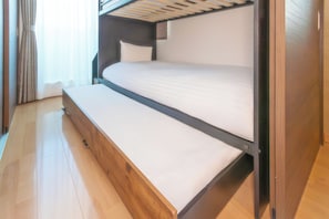 Una cama nido con escritorio extraíble, piso de madera y una ventana con cortinas.