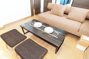 Uma sala de estar moderna com um sofá, duas poltronas, uma mesa de centro e uma mesa de jantar posta com pratos e talheres.