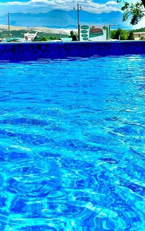 Piscina com água azul cristalina, rodeada por um muro de pedra e vista para montanhas ao longe.