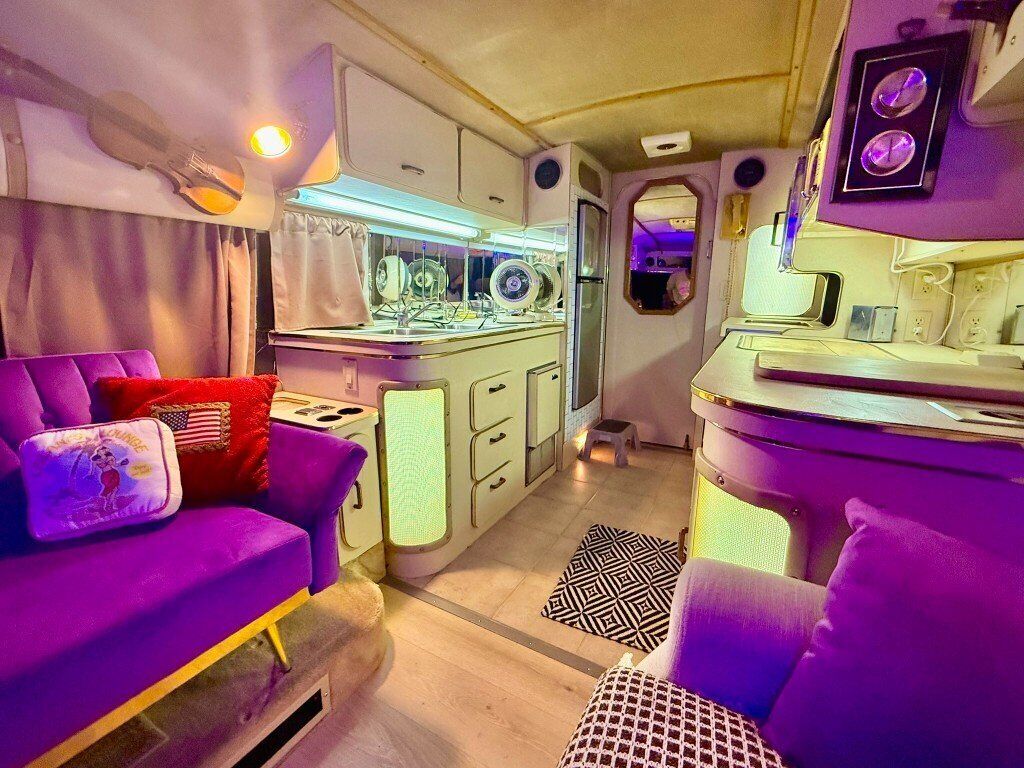 A compact RV interior with a kitchenette, a dining area, and a seating space.