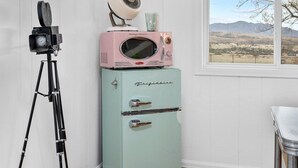 A room with a vintage-style refrigerator, a television mounted on the wall, and a tripod.