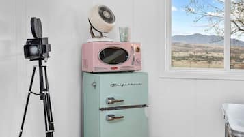 A room with a vintage-style refrigerator, a television mounted on the wall, and a tripod.