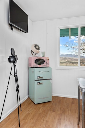 A room with a vintage-style refrigerator, a television mounted on the wall, and a tripod.