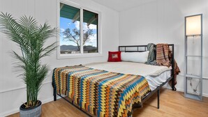 Ein Schlafzimmer mit Bett, Fenster, Topfpflanze und Nachttisch.