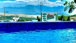A swimming pool with clear blue water, surrounded by a stone wall and a view of distant mountains.