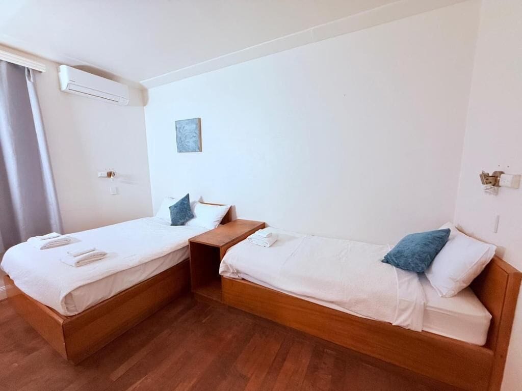 Une chambre avec deux lits simples, des têtes de lit en bois, une petite table et un climatiseur fixé au mur.