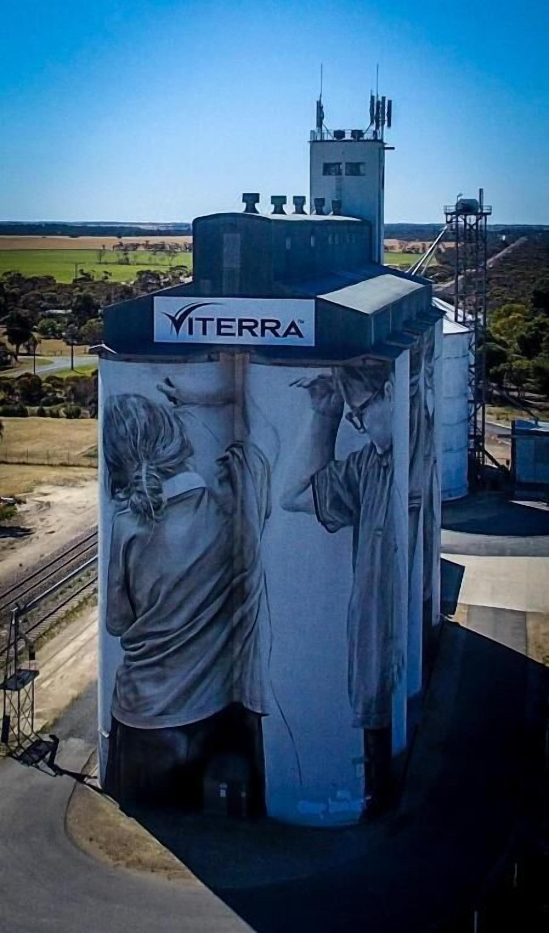 Una gran estructura industrial con un letrero de 'VITERRA', que presenta un mural de dos figuras.