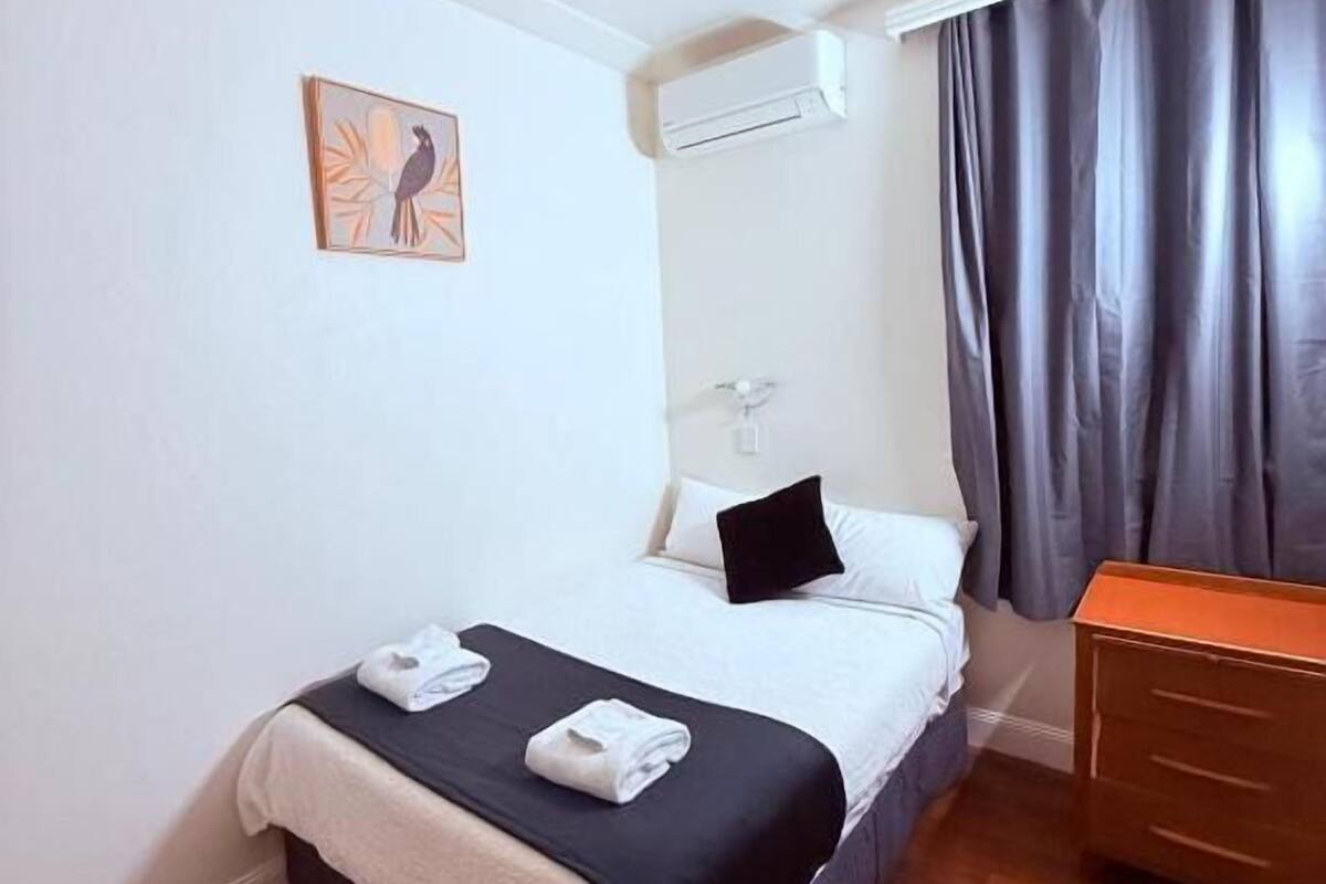 A hotel room with a bed, a dresser, a painting on the wall, and a window with curtains.