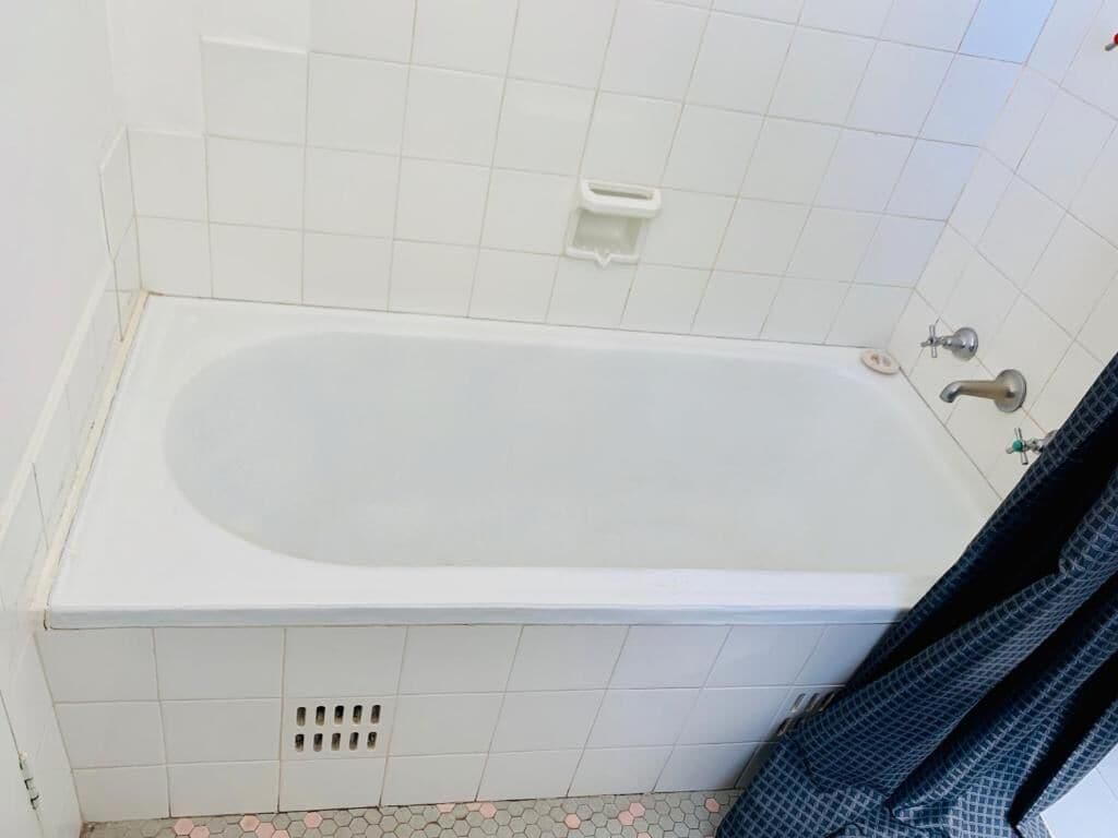 A standard bathtub in a bathroom with white tiles, a showerhead, and a soap dish.