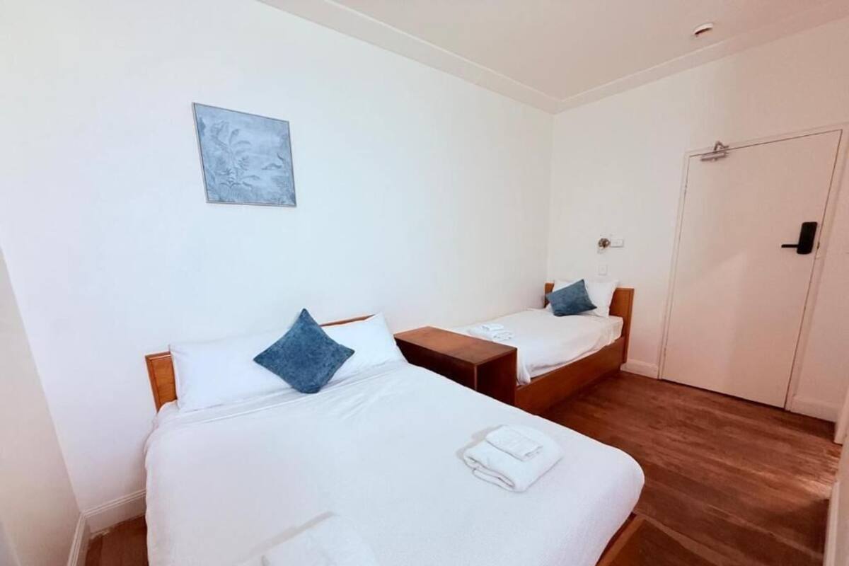 Two single beds with white linens and blue pillows, a wooden floor, a white door, and a small wall-mounted artwork.